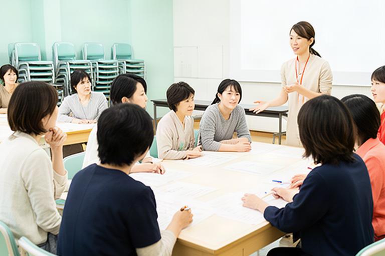学校の多目的室でPTA保護者が教育費の資料を見ながら講座に参加する様子